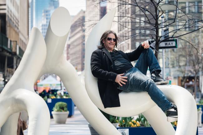 Artist Steve Tobin sitting in a bend of one of his steel sculptures in a relaxed pose. 