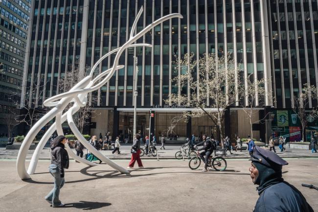 The slender lines of the large white bend backwards on the plaza as people and pigeons walk by. 