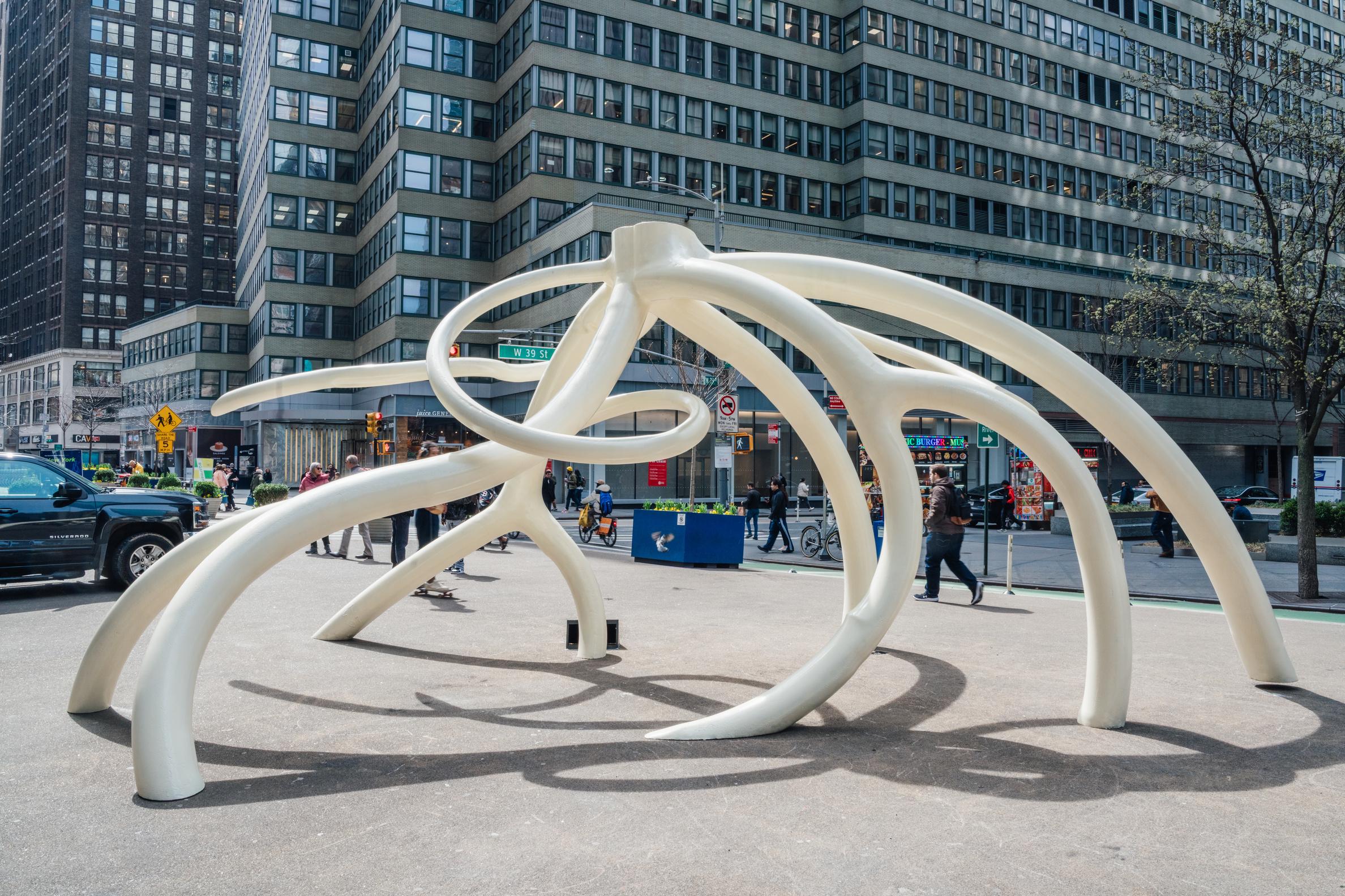 A large white steel sculpture of slender bends and turns resembling roots. 
