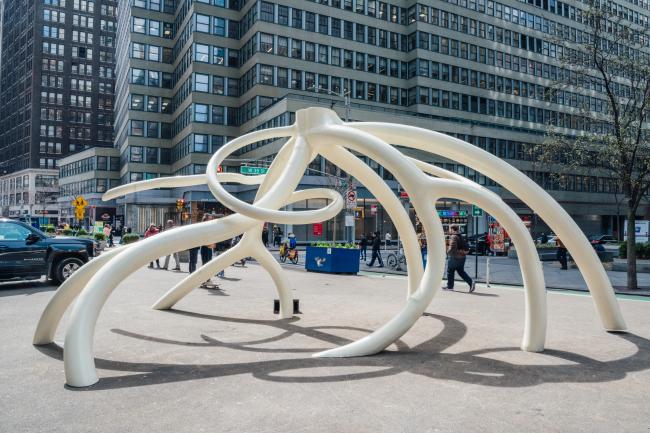A large white steel sculpture of slender bends and turns resembling roots. 