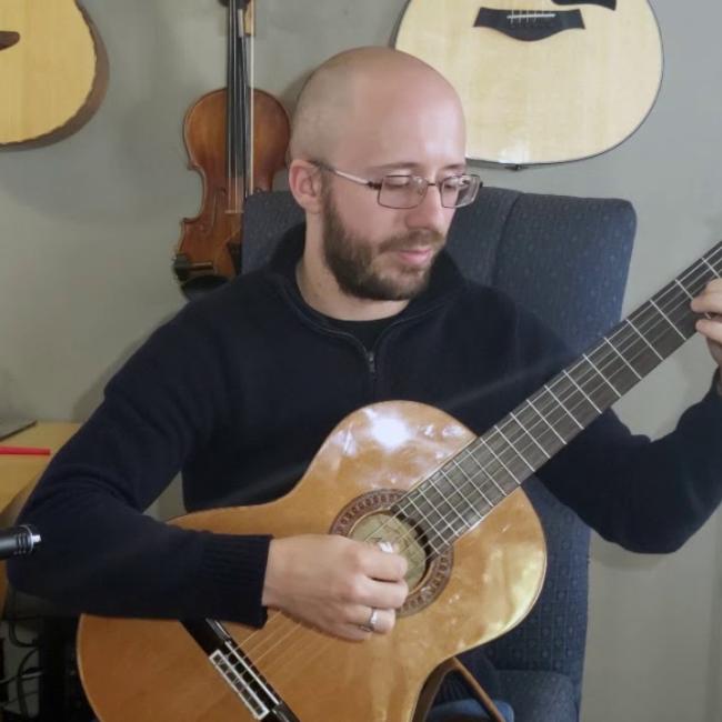 A man sits and skillfully plays an acoustic guitar. 
